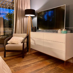 Vista a 45° hacia la izquierda del mueble Cómoda color arena, que tiene seis cajones y cuatro patas metálicas, ambientado en un cuarto.