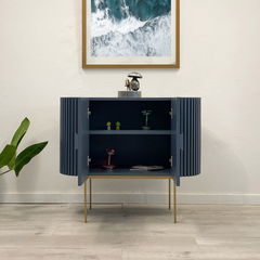 Mueble de almacenamiento azul con puertas de lamas y patas doradas, decorado con una escultura y objetos en su interior.