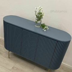 Mueble de color azul con diseño estriado y patas doradas, decorado con un jarrón de vidrio que contiene flores blancas.