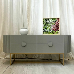 Imagen de  frente del mueble cajonera Bombo, que presenta 4 cajones con tiradores circulares, acompañando la forma de sus extremos, los cuales se encuentran revestidos en madera varillada. Color del mueble: Gris.