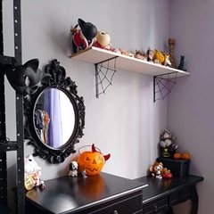 Uma prateleira decorada com figuras de estilo variado, um espelho oval com moldura negra e uma abóbora de Halloween, em um ambiente interno com decoração temática.