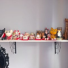 Prateleira com diversas estatuetas de gatos e personagens decorativos em um fundo cinza.