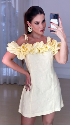 Modelo usando um vestido curto de linho amarelo com babados nos ombros.