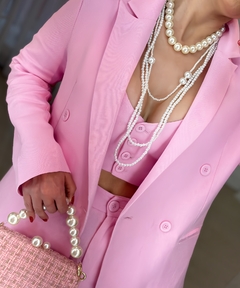 Conjunto rosa com blazer cropped, top e calça, adornado com colares de pérolas e bolsa de tecido.