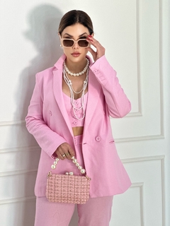 Modelo usando um conjunto de blazer cropped e calça rosa, com acessórios de pérolas e bolsa de palha.