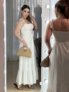 Modelo usando vestido Lavinia de viscolinho, com alças e detalhe em babados, segurando uma bolsa de palha.