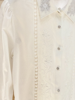 Camisa branca com bordados florais e botões de strass, destacando elegância e detalhe artesanal.