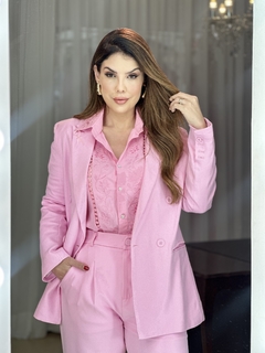 Modelo vestindo a camisa Rafaella bordada com botão de strass, em um conjunto rosa. O fundo apresenta cortinas brancas e um ambiente elegante.