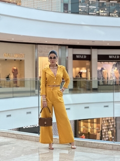 Modelo usando um conjunto de blazer curto e calça de linho amarelo em um shopping moderno.