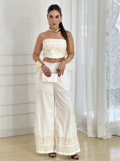 Mulher usando um conjunto Caribe com top cropped branco e calça larga, adornada com detalhes em dourado.