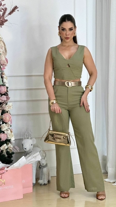 Modelo usando um conjunto de cropped e calça pantalona em linho na cor verde, com acessórios dourados e uma bolsa dourada, em ambiente decorado para festas.