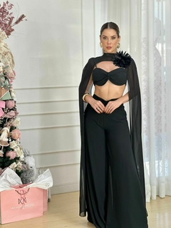 Modelo vestindo o conjunto Angelane Flor, que consiste em um top preto com detalhes e calças largas, em frente a uma árvore decorada.