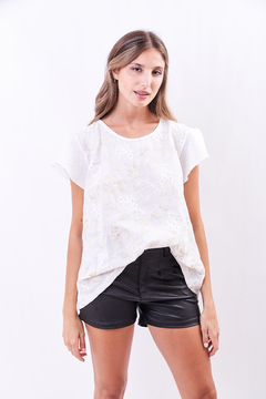 Blusa amplia, con flores bordadas blancas y doradas.