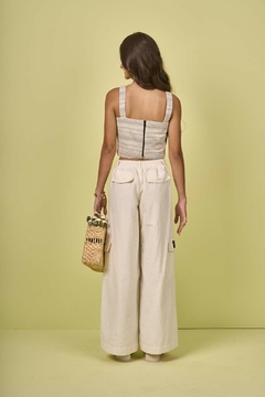 Modelo de costas usando conjunto juvenil com calça wide leg off white e top mescla com preto, segurando uma bolsa de palha.