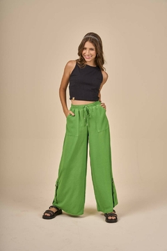 Modelo feminina vestindo blusa juvenil em malha canelada preta e calça verde, com um sorriso no rosto.