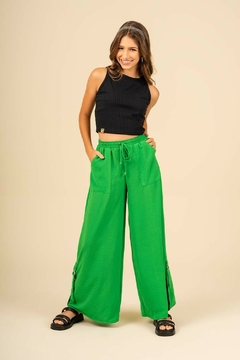 Modelo jovem usando calça wide leg verde em crepe, com blusa preta e sandálias.