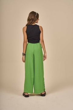 Modelo de costas usando calça juvenil wide leg em crepe na cor verde, combinada com um top preto, em fundo claro.