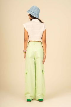 Modelo de calça juvenil em sarja wide leg cargo na cor verde claro, vista de trás, com blusa cropped e chapéu azul.