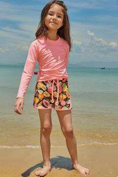 Menina sorrindo na praia usando blusa infantil rosa em malha UV Dry com proteção UV50+