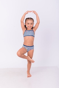 Menina brincando com um biquíni listrado, posando de forma divertida com uma perna levantada.