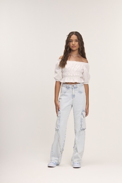 Modelo usando blusa branca off-shoulder e calça jeans clara com detalhes cargo.