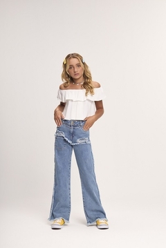 Modelo usando uma blusa cropped branca e calça jeans rasgada, com acessórios coloridos no cabelo.