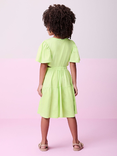 Vestido verde com aberturas laterais, vista traseira, usado por uma menina com cabelo cacheado.