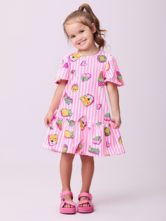 Menina sorridente vestindo um vestido rosa listrado com ícones coloridos, incluindo frutas e emojis.