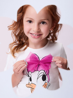 Menina sorridente segurando um laço de tule rosa na blusa com estampa da personagem Daisy Duck.