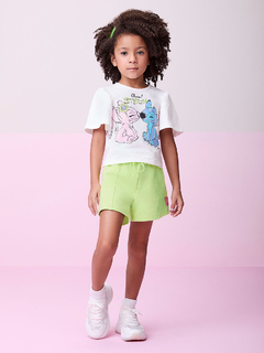 Menina de cabelos cacheados usando um conjunto de blusa branca com estampa do Stitch e short verde-limão.