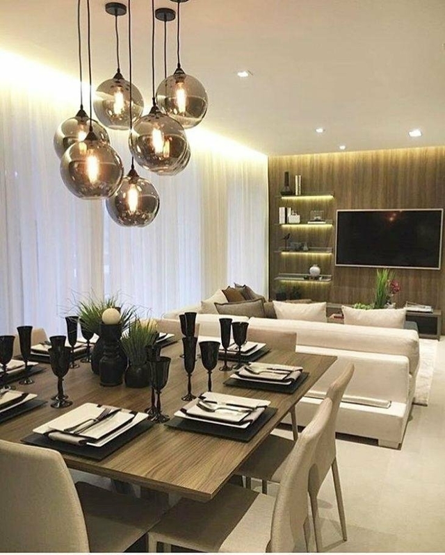Imagem de uma sala de jantar moderna com uma mesa de madeira escura, decorada com pratos e taças pretas, e luminárias pendentes fumê espelhadas ao fundo.
