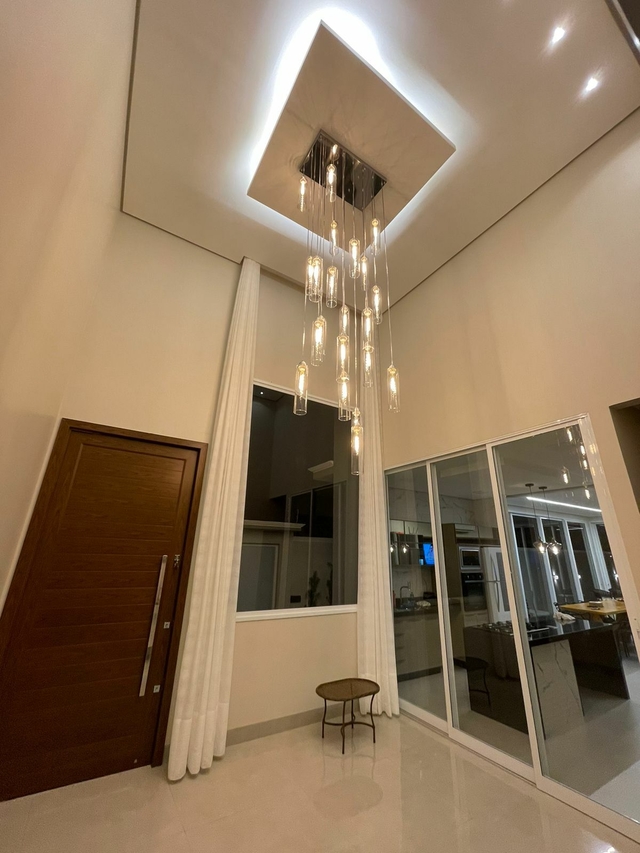 Imagem do lustre da Linha Dunáh em vidro transparente, pendurado no teto de um ambiente moderno e iluminado.