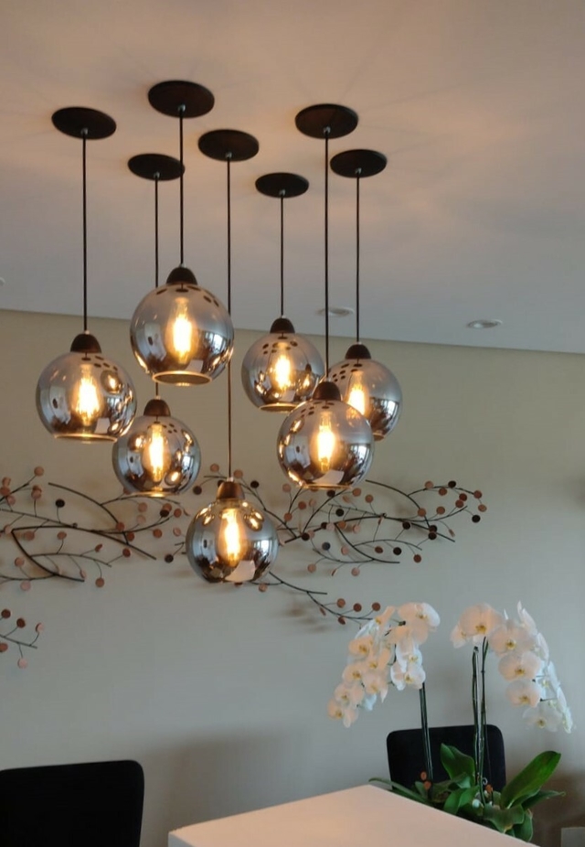 Iluminação pendente da Linha Sarvah Fumê Espelhado com lâmpadas em formato esférico, em ambiente moderno com orquídeas brancas ao fundo.