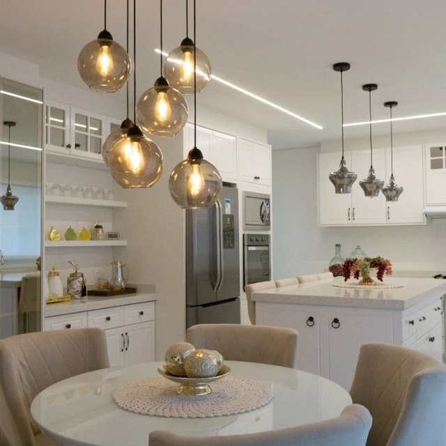 Ambiente moderno com luminárias pendentes de vidro fumê sobre uma mesa de jantar redonda, destacando a decoração minimalista da cozinha.