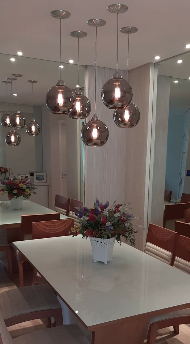Iluminação pendente da linha Sarvah Fumê Espelhado em uma sala de jantar, com mesa branca e arranjo de flores coloridas.