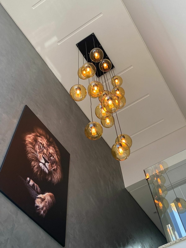 Ambiente moderno com parede cinza, lustre pendente de esferas âmbar e quadro de leão em destaque.