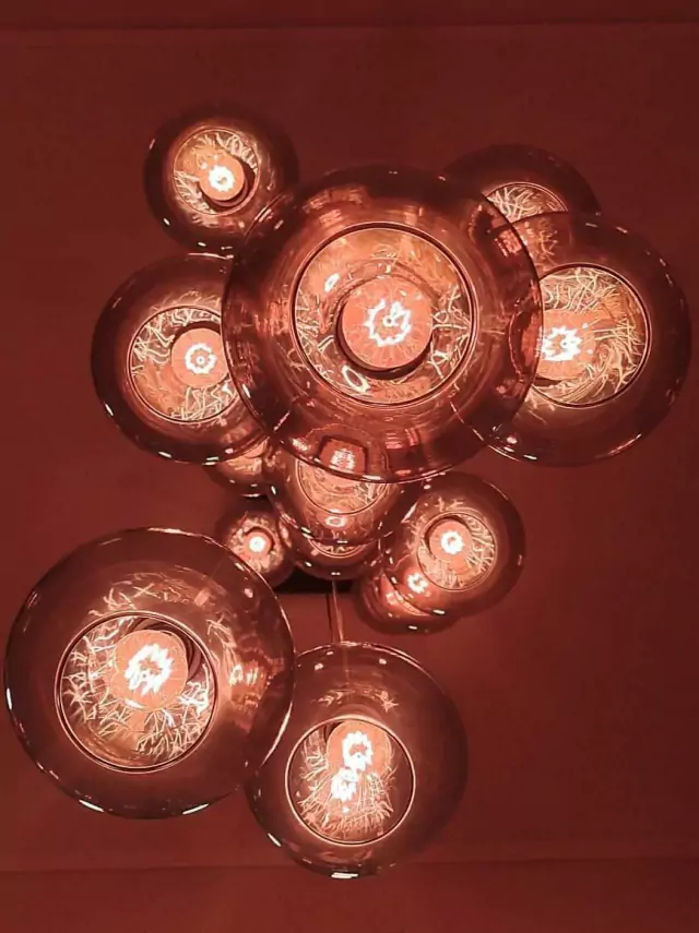 Lustre com design moderno, composto por várias esferas de vidro fumê, iluminadas por lâmpadas internas, criando um efeito visual impactante.