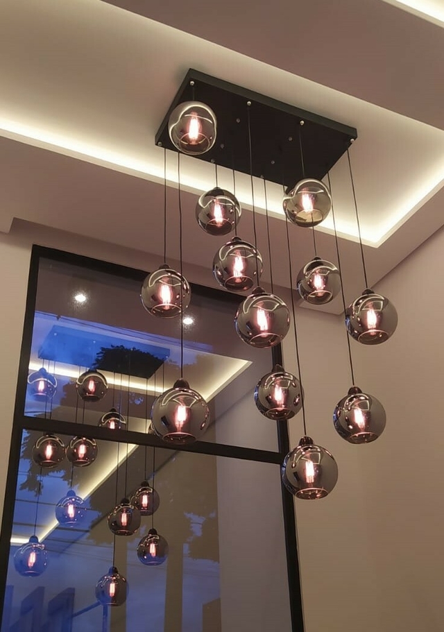 Lustre moderno da Linha Sarvah com vidros fumê espelhados pendendo do teto, iluminando um ambiente elegante.