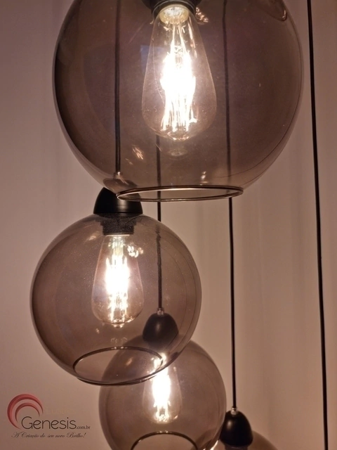Três lâmpadas pendentes em globos de vidro fumê, iluminando o ambiente com um design moderno.