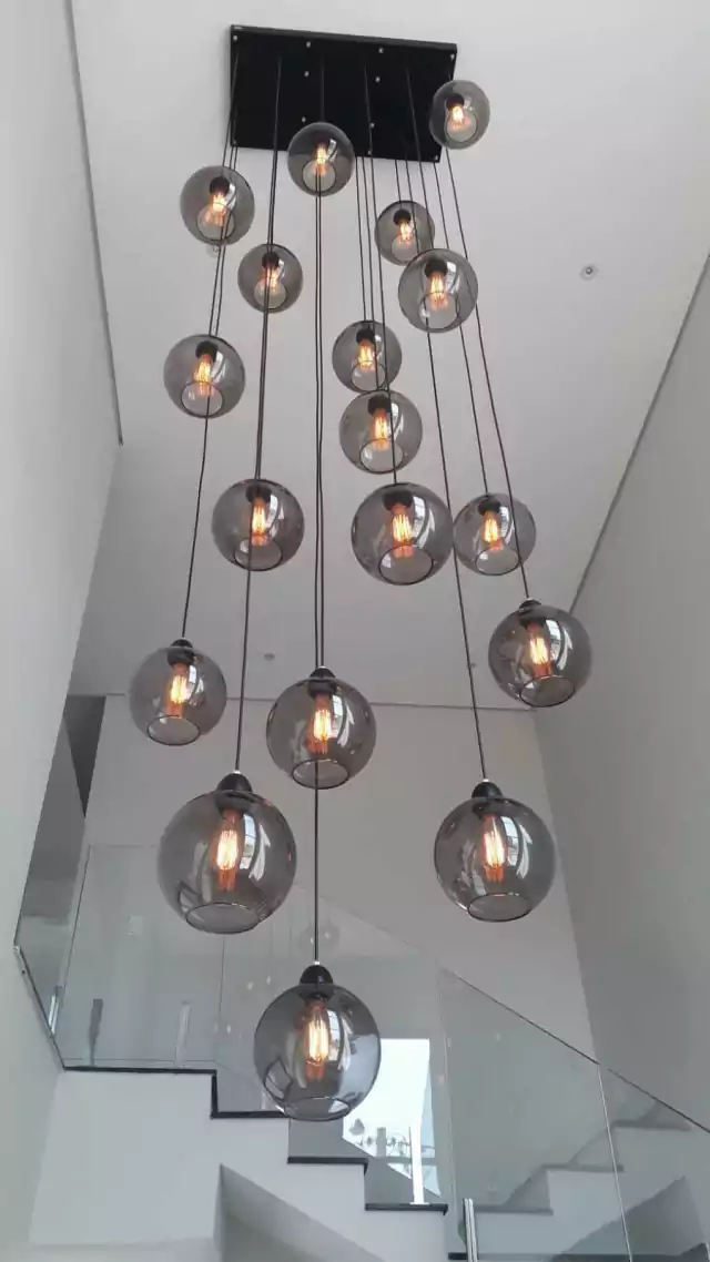 Um lustre moderno com várias lâmpadas em globos de vidro fumê, pendurado em um teto alto.
