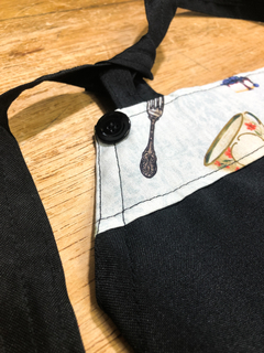 Avental frontal preto em oxford com estampa em tricoline Amarração no pescoço ajustável em nó Bolso no centro 