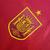 Emblema da Seleção da Espanha em uma camisa vermelha, com detalhes em amarelo e uma estrela acima.