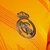 Detalhe do escudo do Real Madrid na camisa laranja 24/25 da Adidas para torcedores.