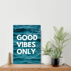 Placa sobre prateleira com o dizer good vibes only com oceano azul ao fundo. Formato retangular.