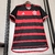 Camisa de futebol do Flamengo, com listras vermelhas e pretas, pendurada em um cabide.