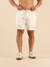 Homem usando shorts de linho curto na cor off white, com tênis brancos, em fundo claro.