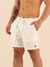 Modelo masculino usando shorts curtos de linho off white com bolso e cordão na cintura.