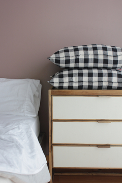 Almohadón Laurel con diseño a cuadros en blanco y negro sobre una cama con sábanas blancas y una lámpara de mesa de estilo moderno.