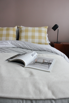 Almohadones de cuadros amarillos y blancos sobre una cama con una manta gris y una revista abierta.