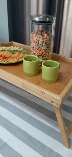 Bandeja de bambú con patas, decorada con tazas verdes y un frasco de cereales coloridos.